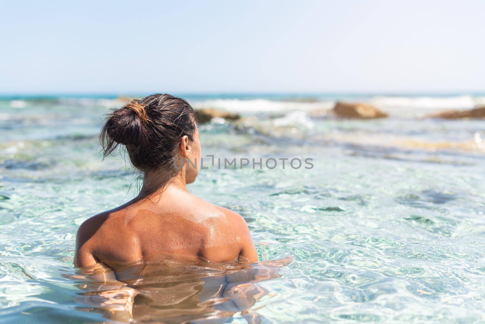 Back view of unrecognizable naked female swimming in clear sea water on sunny day on nude beach on Formentera island