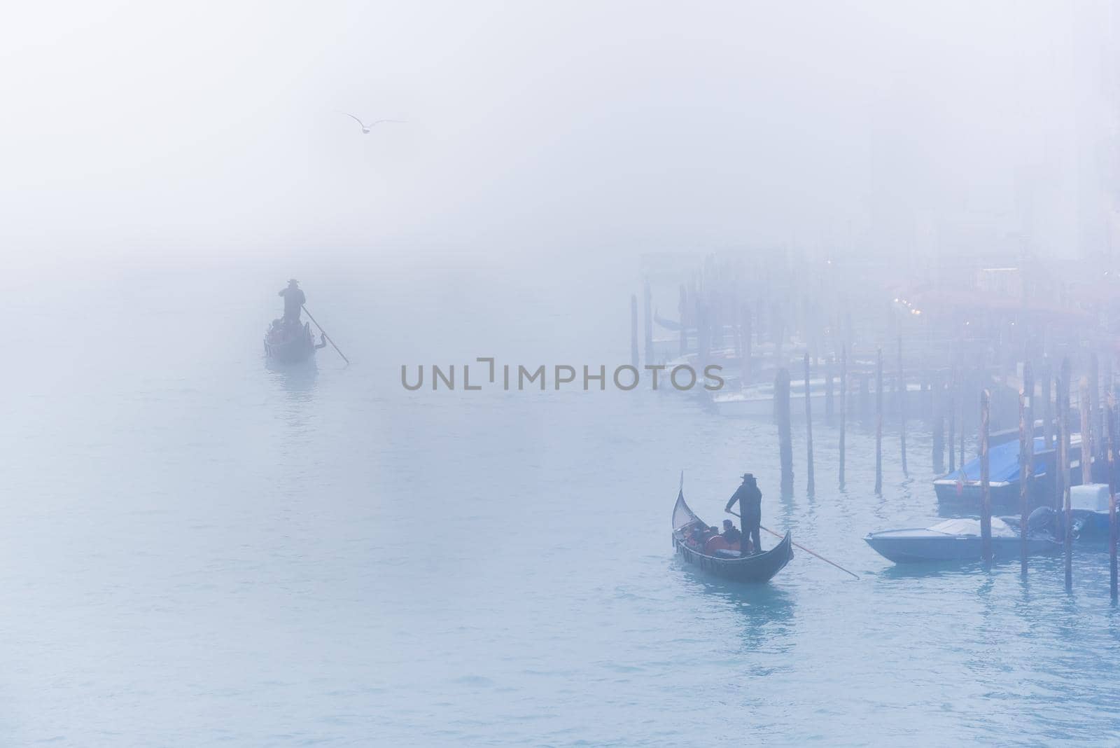 Distant unrecognizable gondolier carrying tourists in wooden boats on rippling canal water in hazy day in Venice