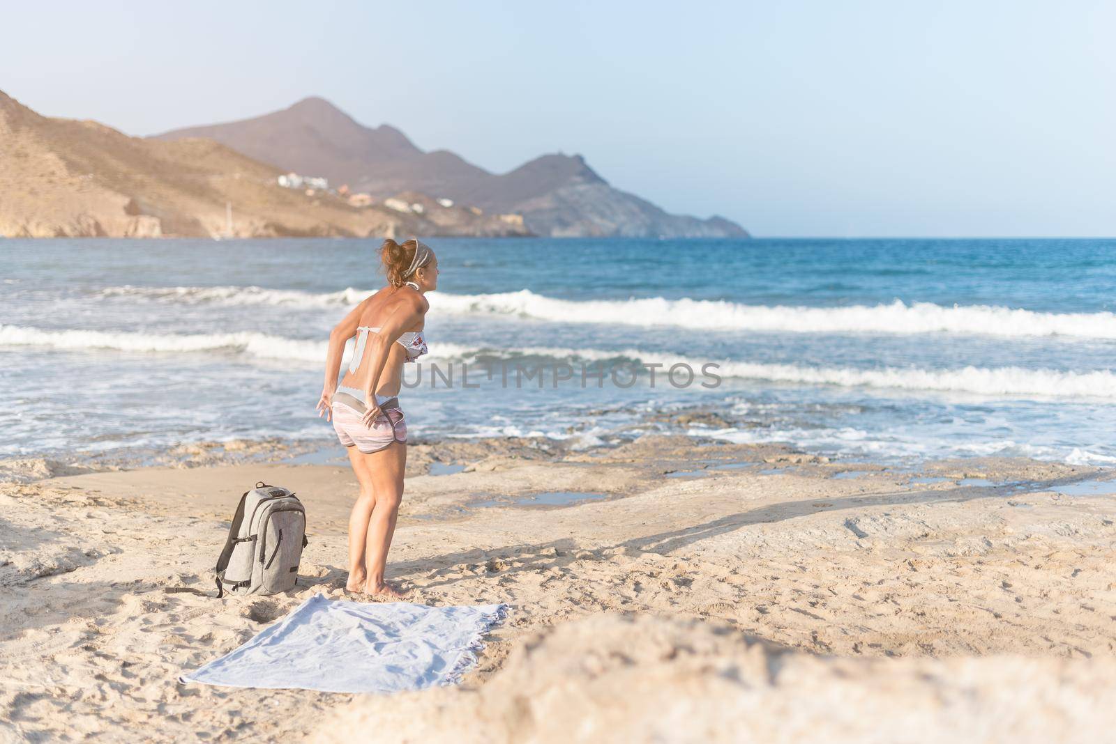 Anonymous woman on sandy beach near waving sea by ivanmoreno