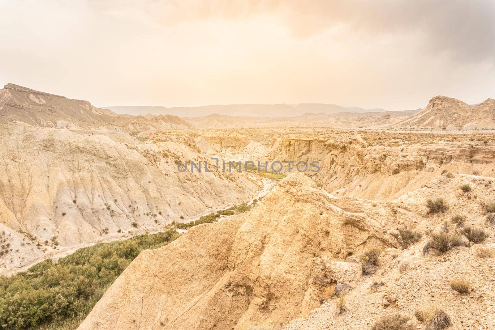 Picturesque drone view of sandy mountain range covered with verdant plants against cloudy sky in daylight in Tabernas desert