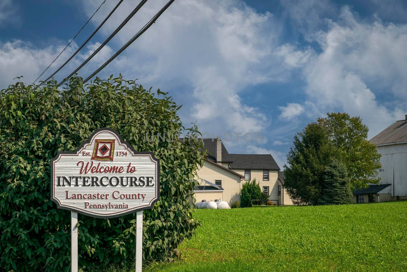 A Welcome Sign to Intercouse, on the Road Next to Brushes and Grass on a Sunny Day