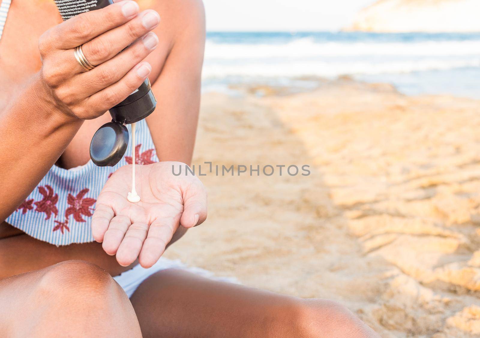 Crop unrecognizable female in swimwear applying sunscreen while resting on sandy beach near waving sea during summer vacation in Spain