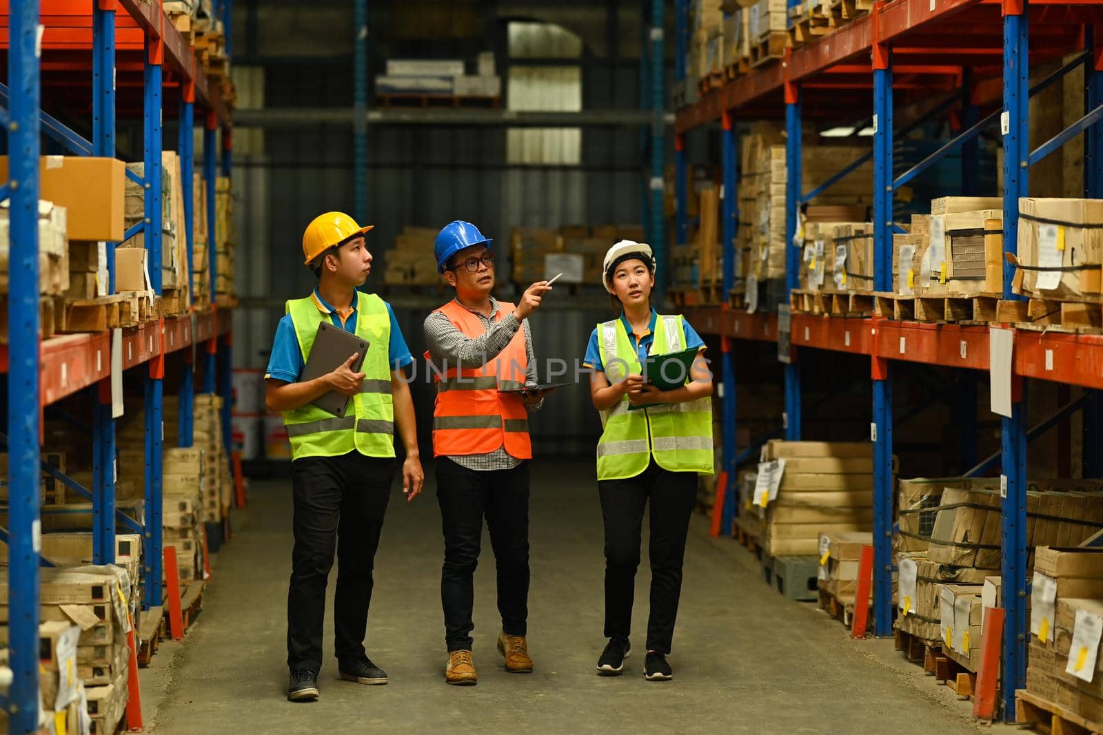 Senior male managers and storehouse employees are checking inventory in a warehouse with shelves full of cardboard boxes by prathanchorruangsak