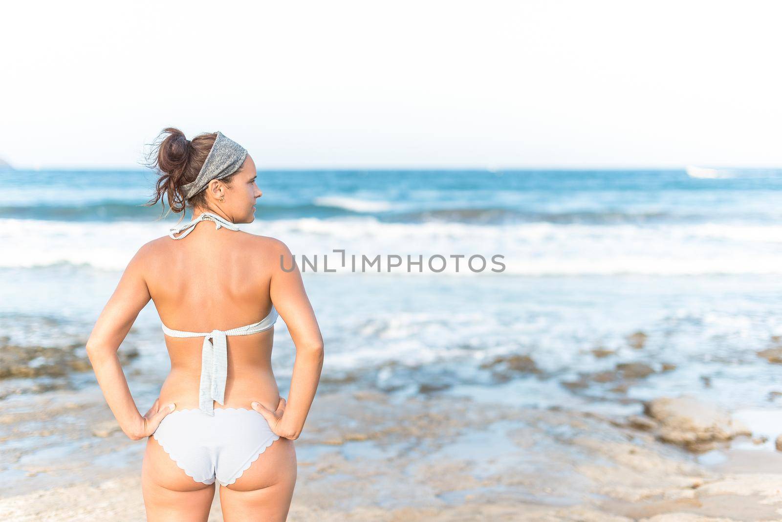 Back view of young female tourist wearing swimwear looking away and contemplating sea view while enjoying sunny vacation day in Almeria Andalusia Spain