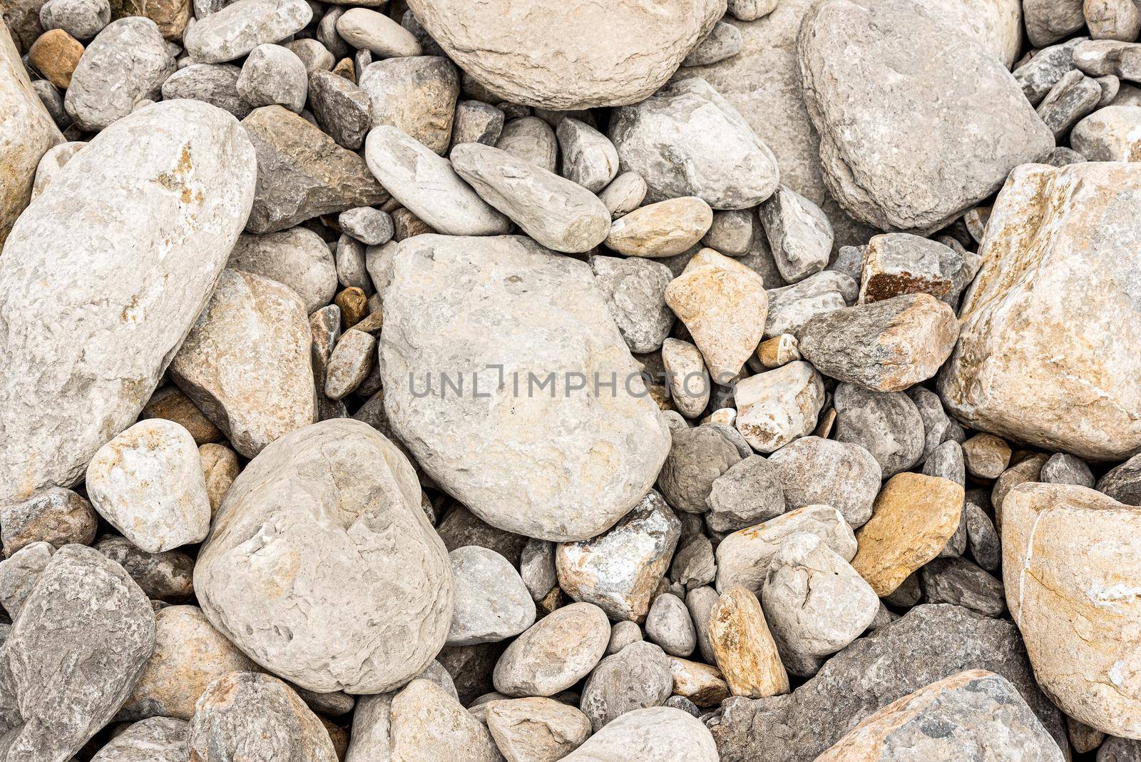 From above background of various shapes dry scattered gray stones on shore in sunlight