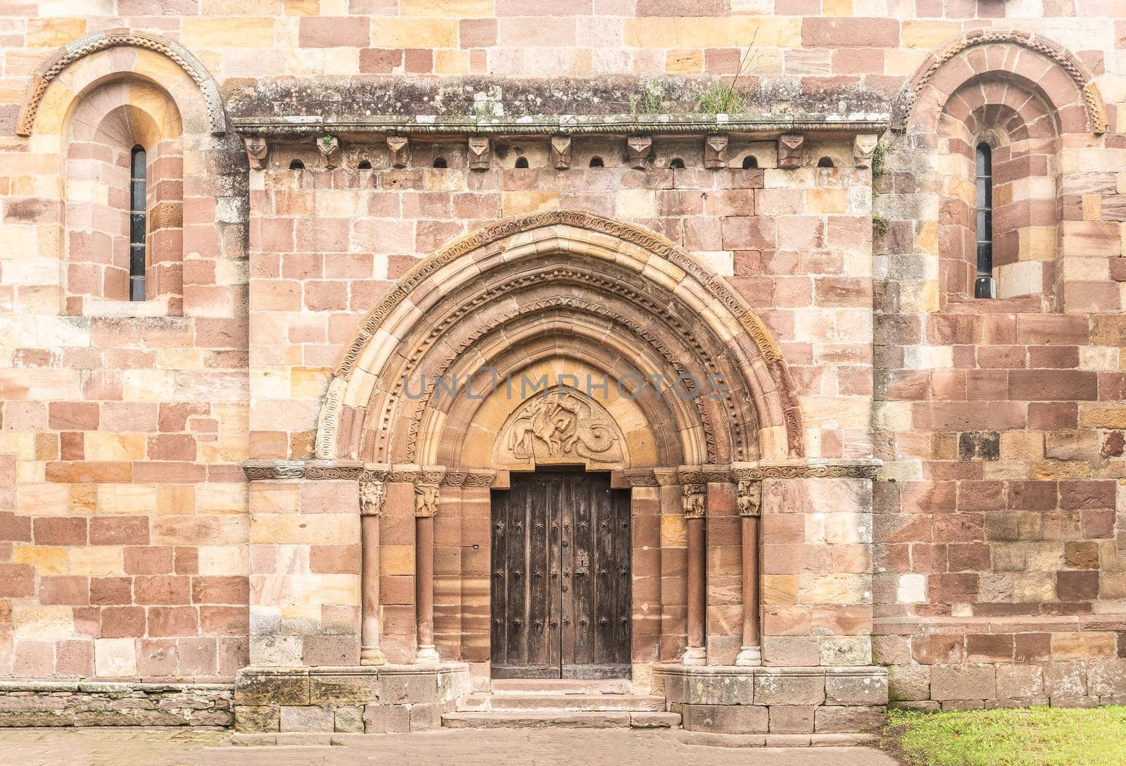 Exterior view of aged stone Romanesque church entrance with arched doorway and ornamental brick walls in Spain in Cantabria