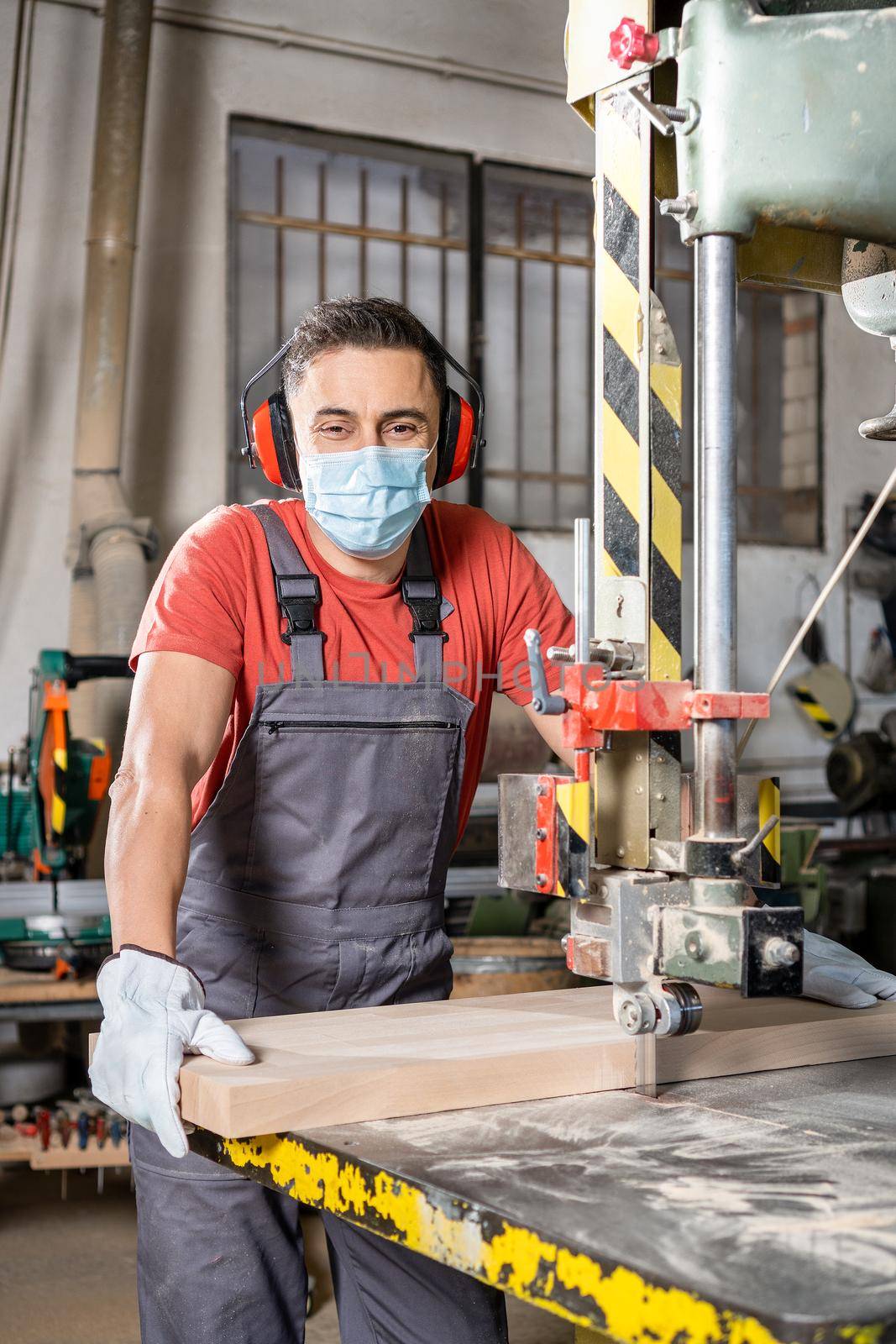 Worker in mask cutting plank on band saw by ivanmoreno