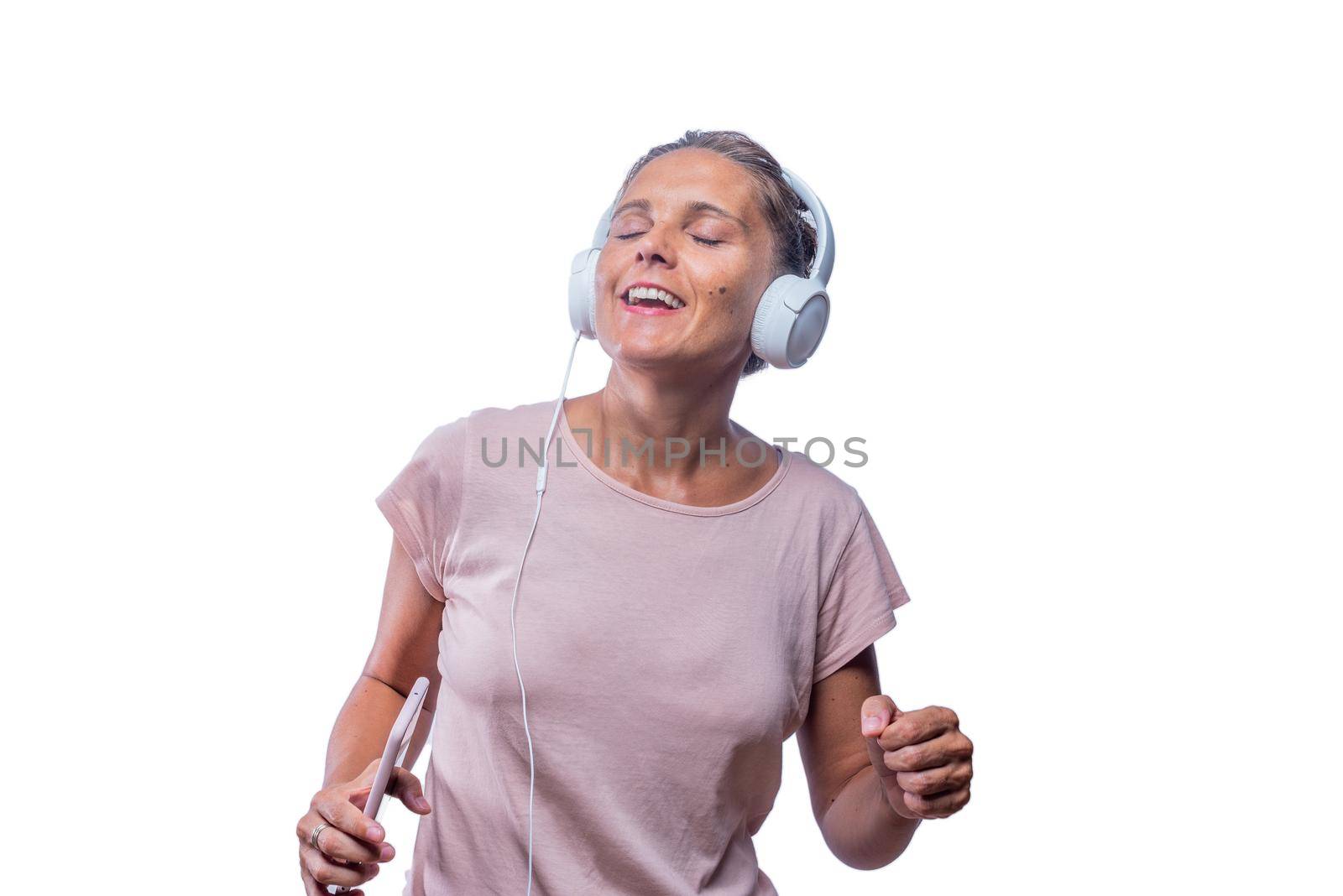adult woman enjoying listening to music and dancing with her smartphone with her eyes closed on a white background with copy space.