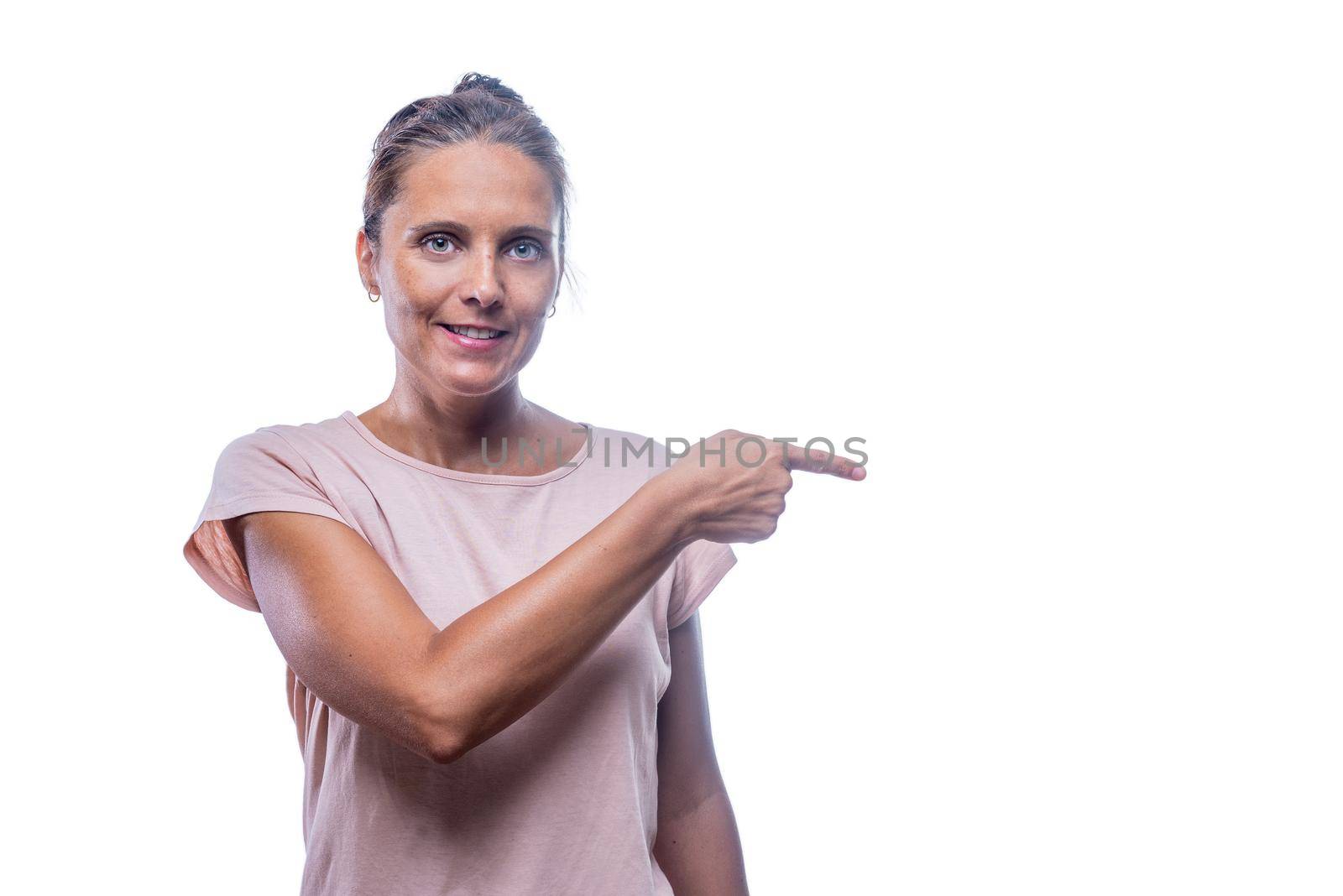 Front view of a smiling green-eyed woman pointing with her finger to something while looking at camera on a white background with copy space.