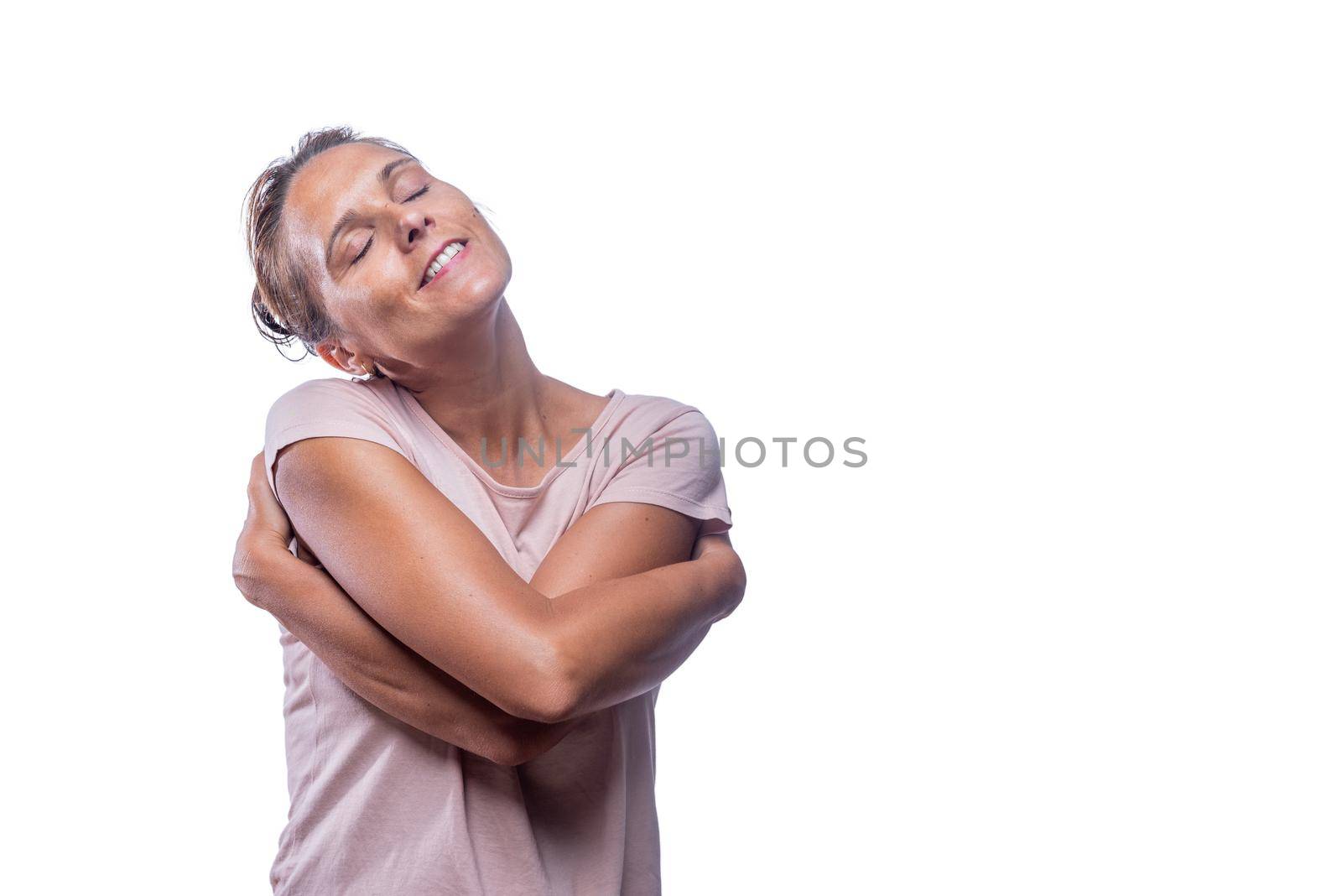 Front view of a green-eyed tender romantic woman embraces own body, hugs herself with eyes closed on a white background with copy space. Concept i love myself.