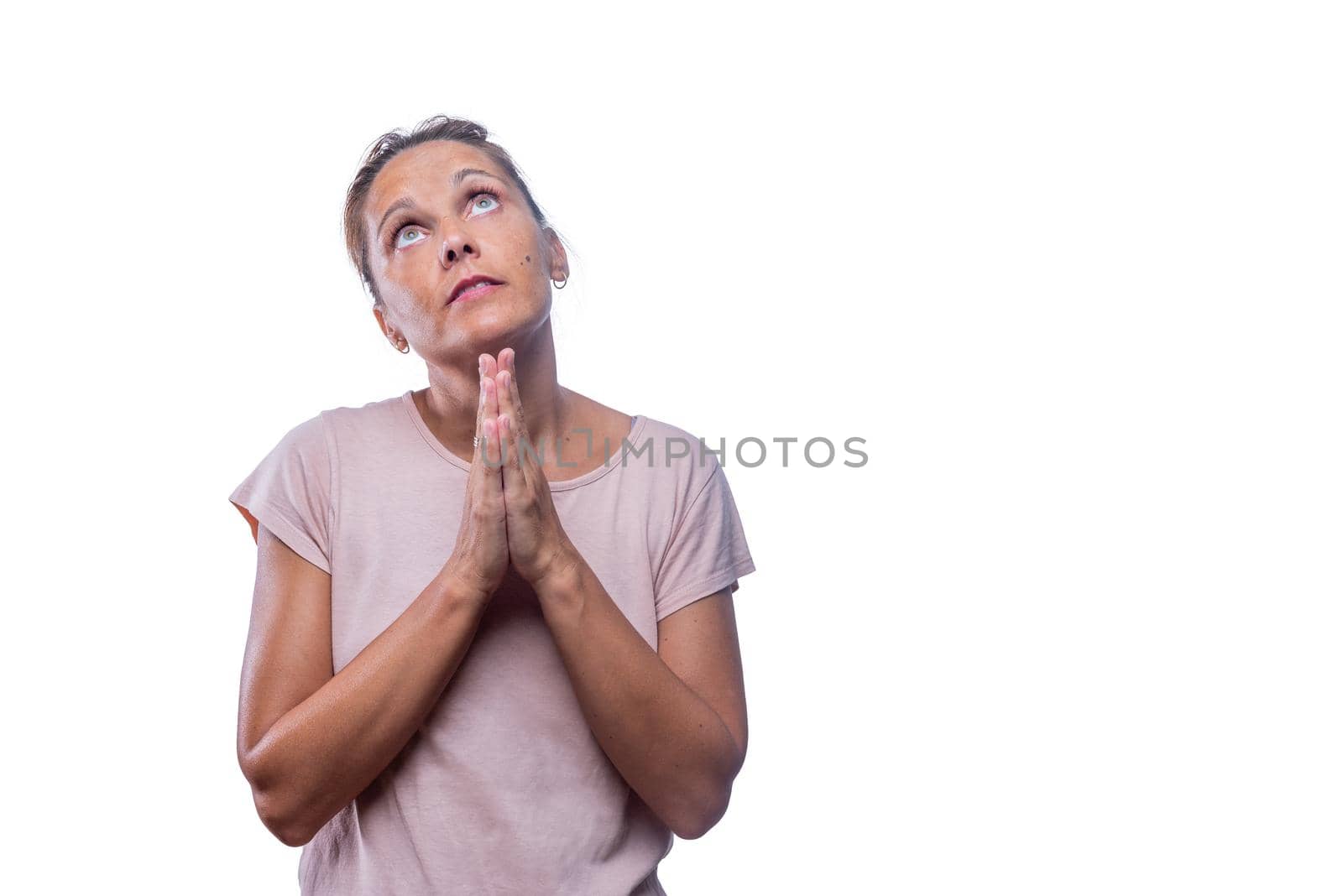 Front view of a devoted adult woman looking up praying with hands clasped on a white background with copy space.