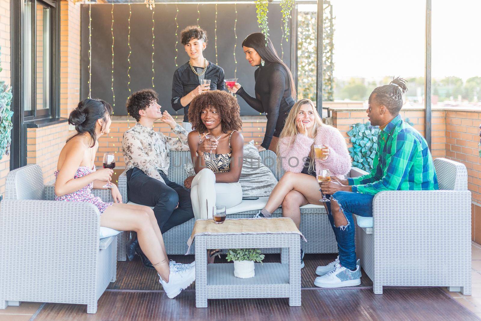 A group of multiethnic friends sitting on a terrace drinking and having a good time in a party.