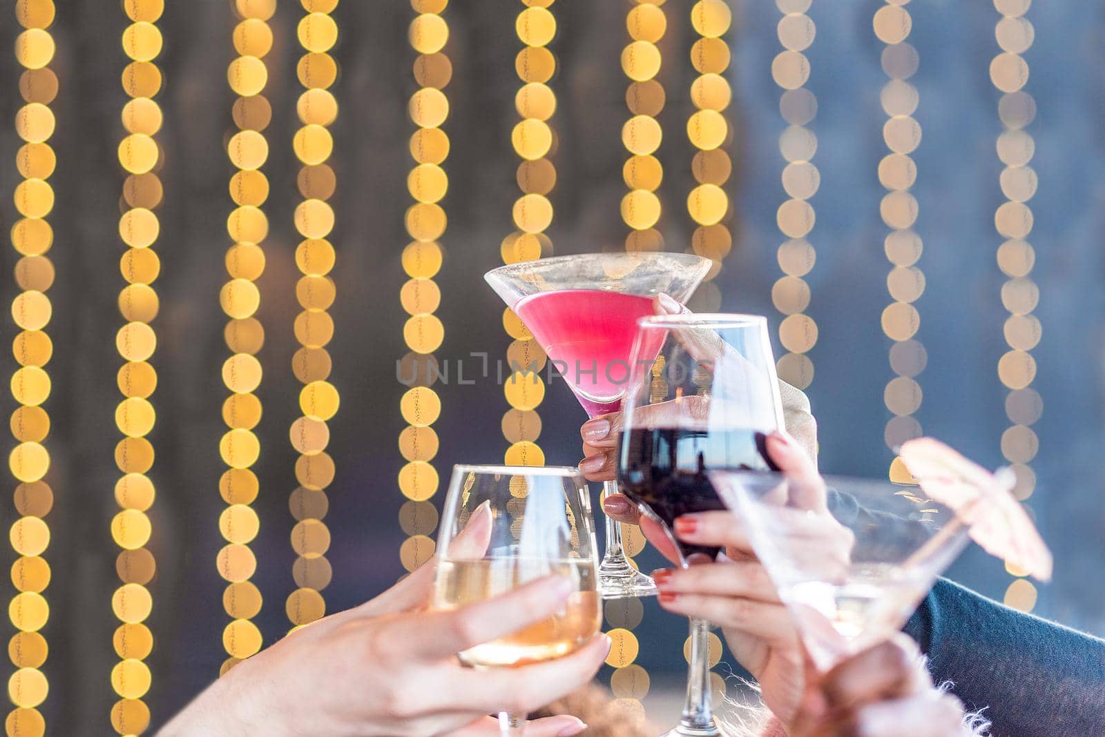 Close-up of hands holding drinks and cocktails toasting against a background of blurred lights.