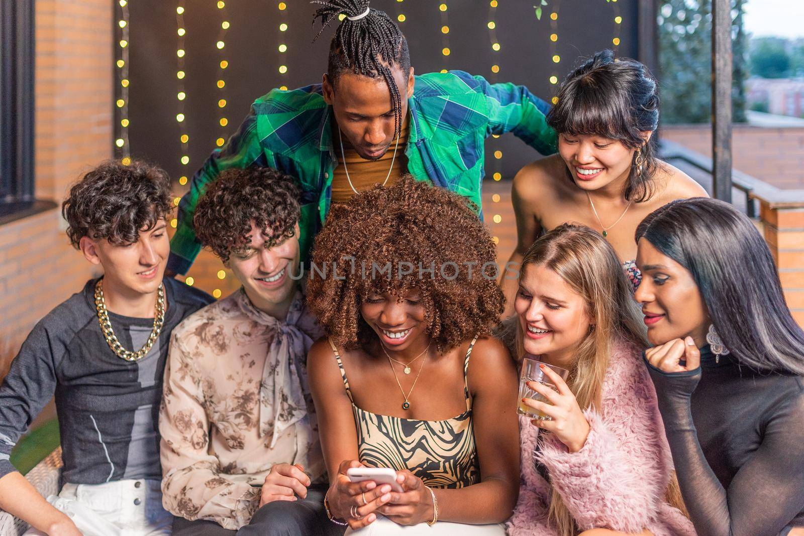 A group of multi-ethnic friends looking to a phone on a terrace while drinking