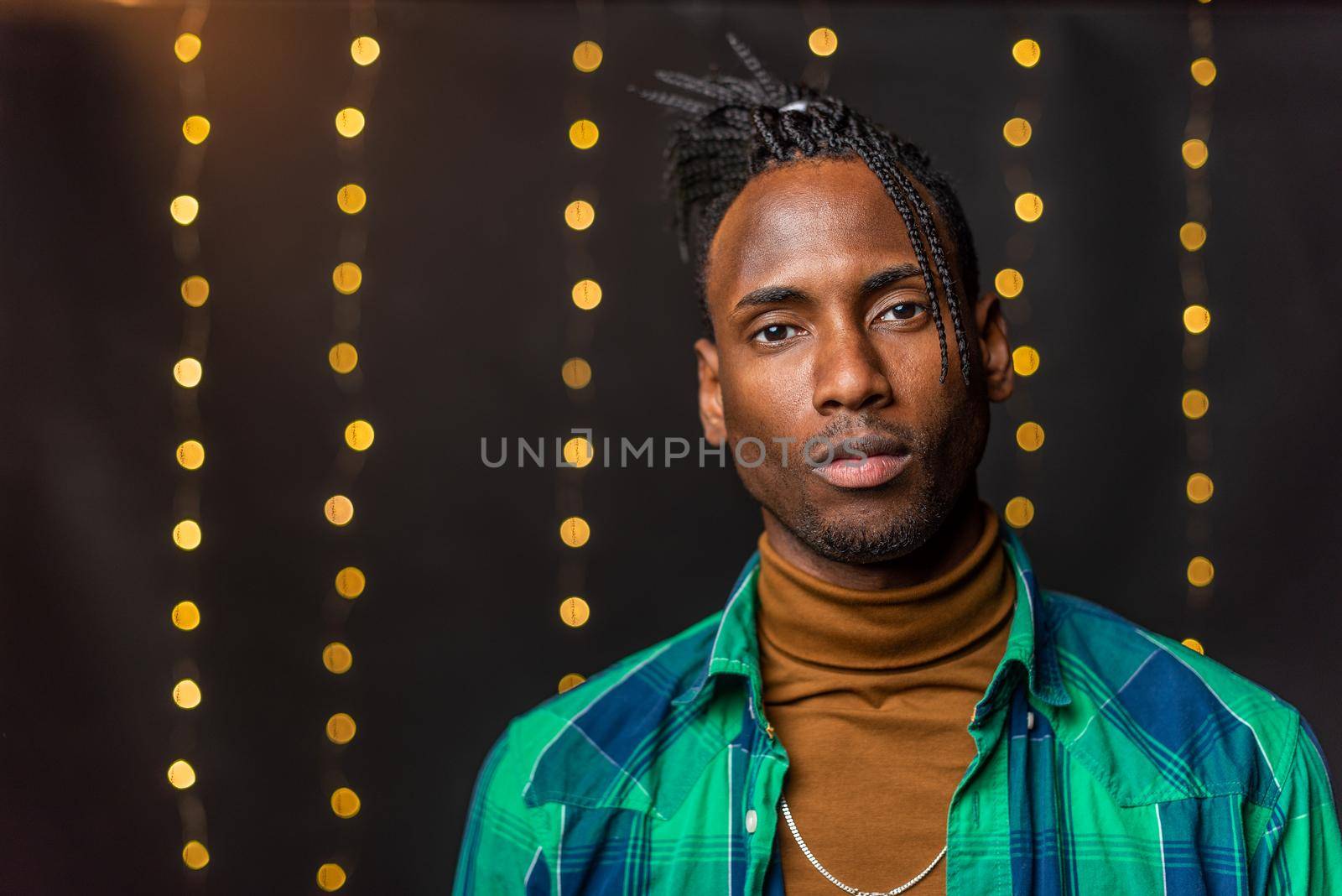 Portrait of a serious young African American with braids looking at the camera with a blurred light background.