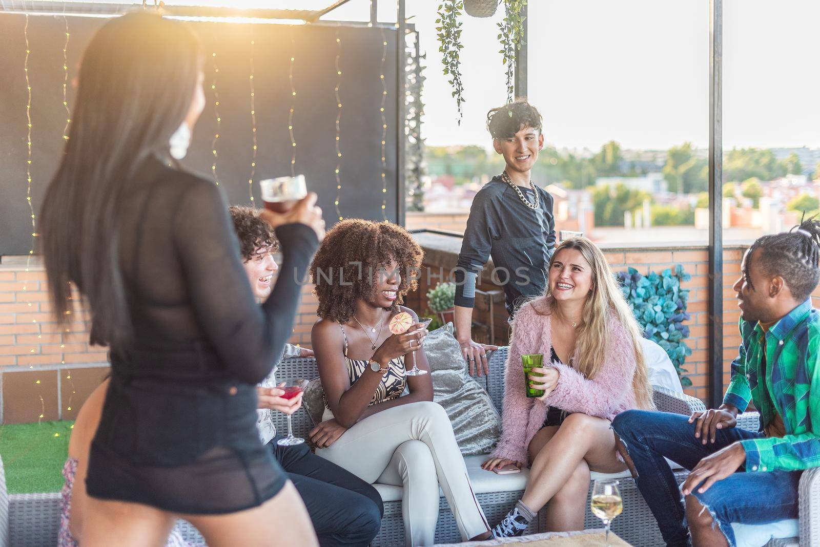A happy group of multiethnic friends sitting on a terrace drinking and having a good time in daytime.