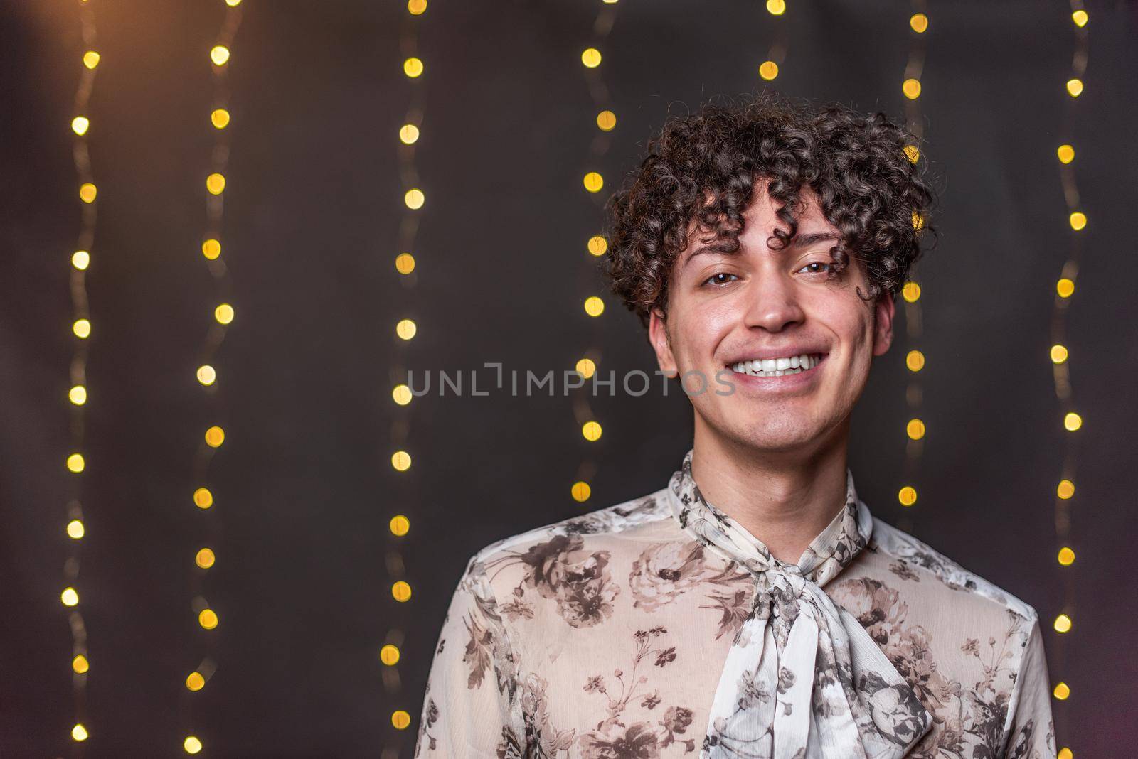 Portrait of young gay man looking at camera and smiling with a blurred light background in New Year's Eve with copy space