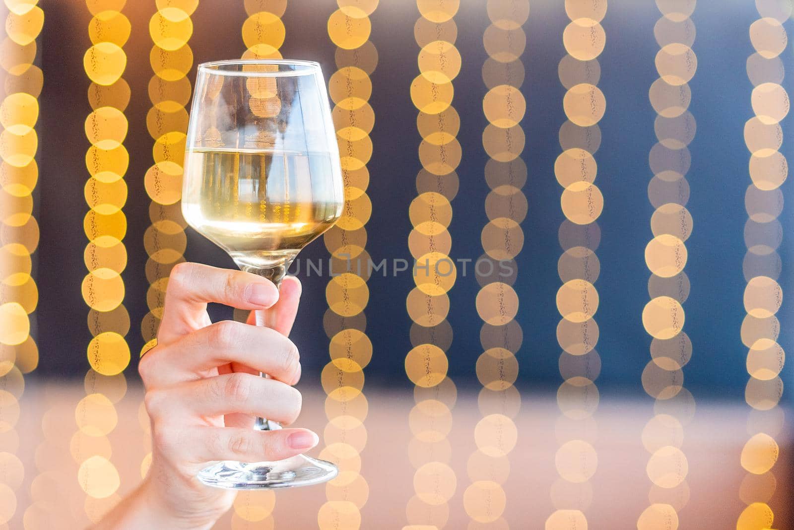 A hand holding a glass with white wine on blurred background with copy space.