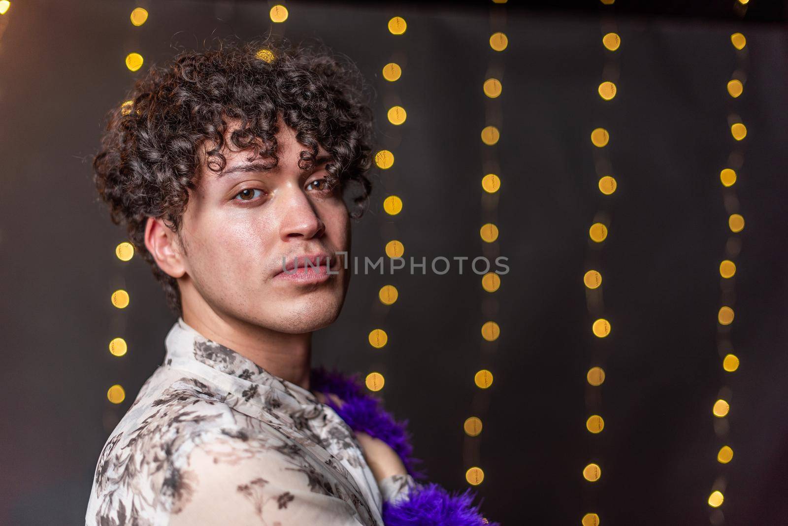 Portrait of young gay man standing sideways looking at the camera with a blurred light background in New Year's Eve with copy space