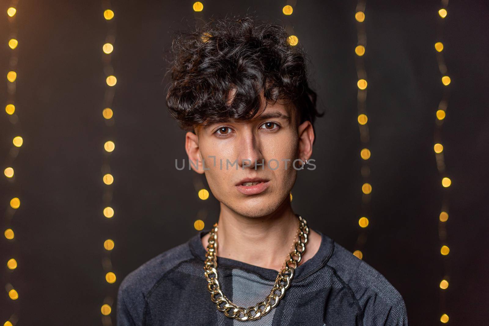 Portrait of a young man looking at the camera without smiling with a gold-colored chain around his neck with a blurred light background
