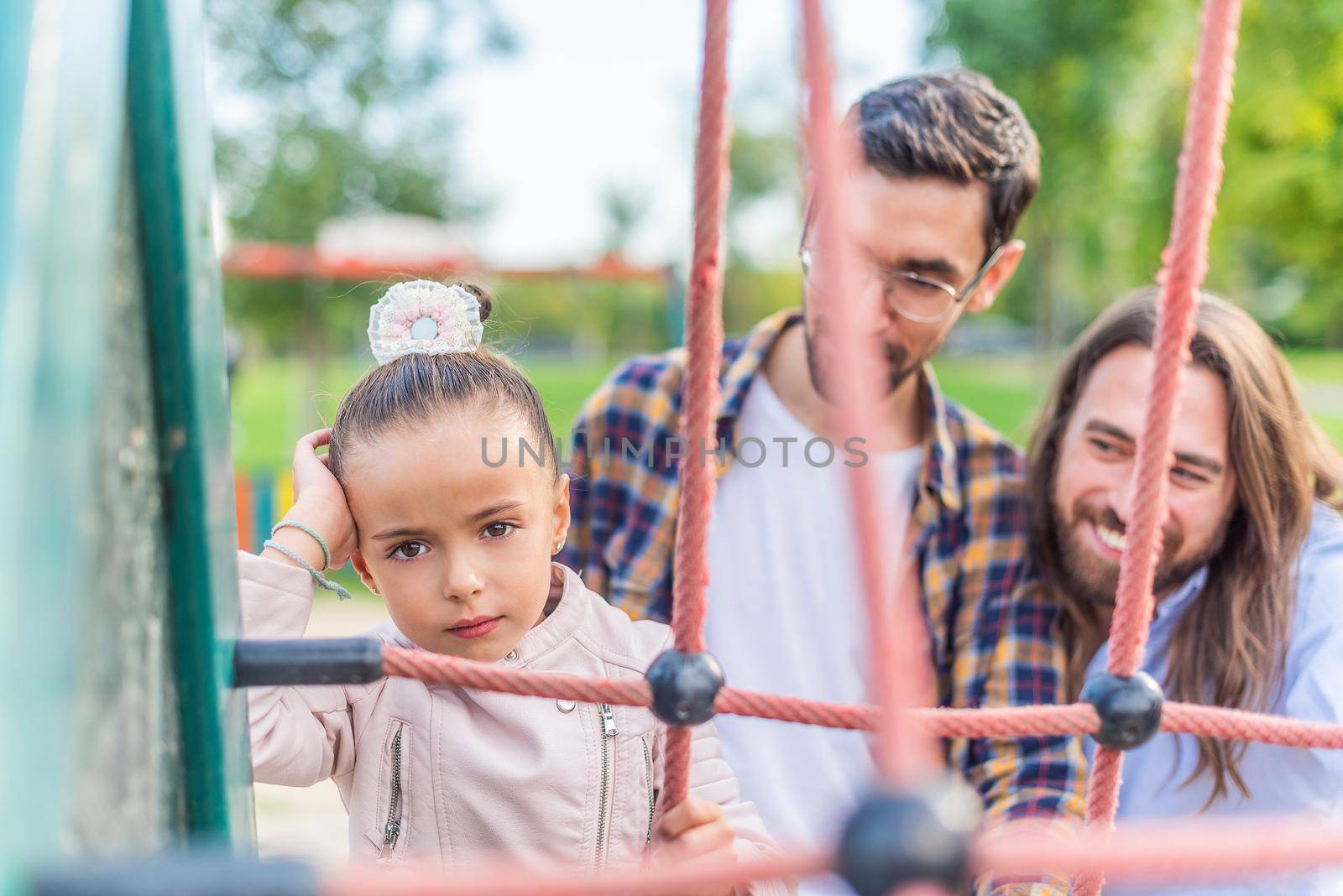 Girl in playground with her parents looking at camera unhappy. by ivanmoreno