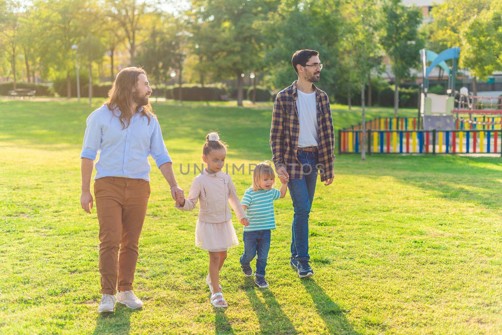 Full length view of a gay male couple with their two adopted children strolling in the park on a sunny day.