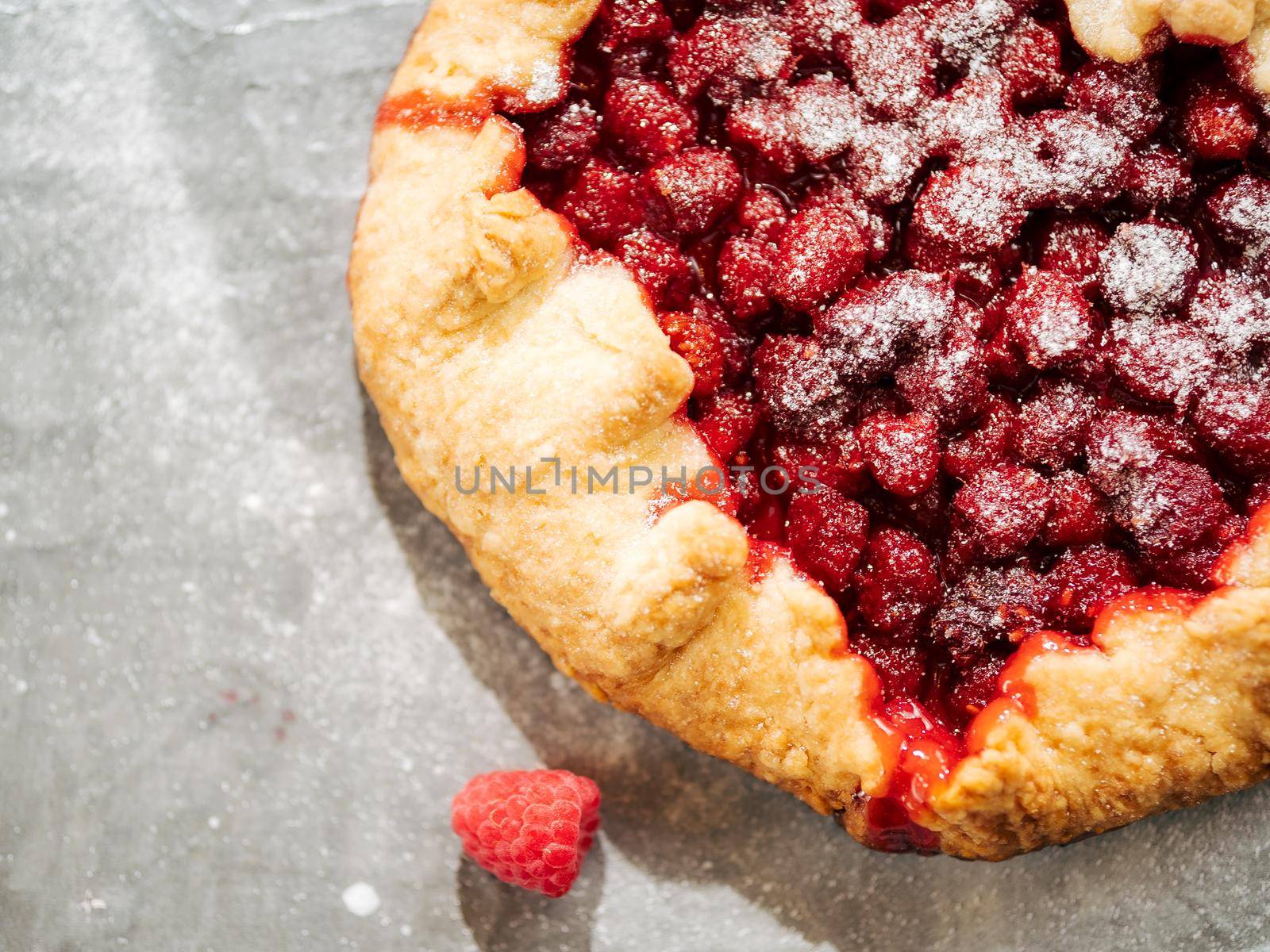 Perfect raspberry galette. Delicious rustic homemade tart with frozen or fresh raspberries on gray textured background. Beautiful round shape galette with raspberries,copy space. Top view or flat lay