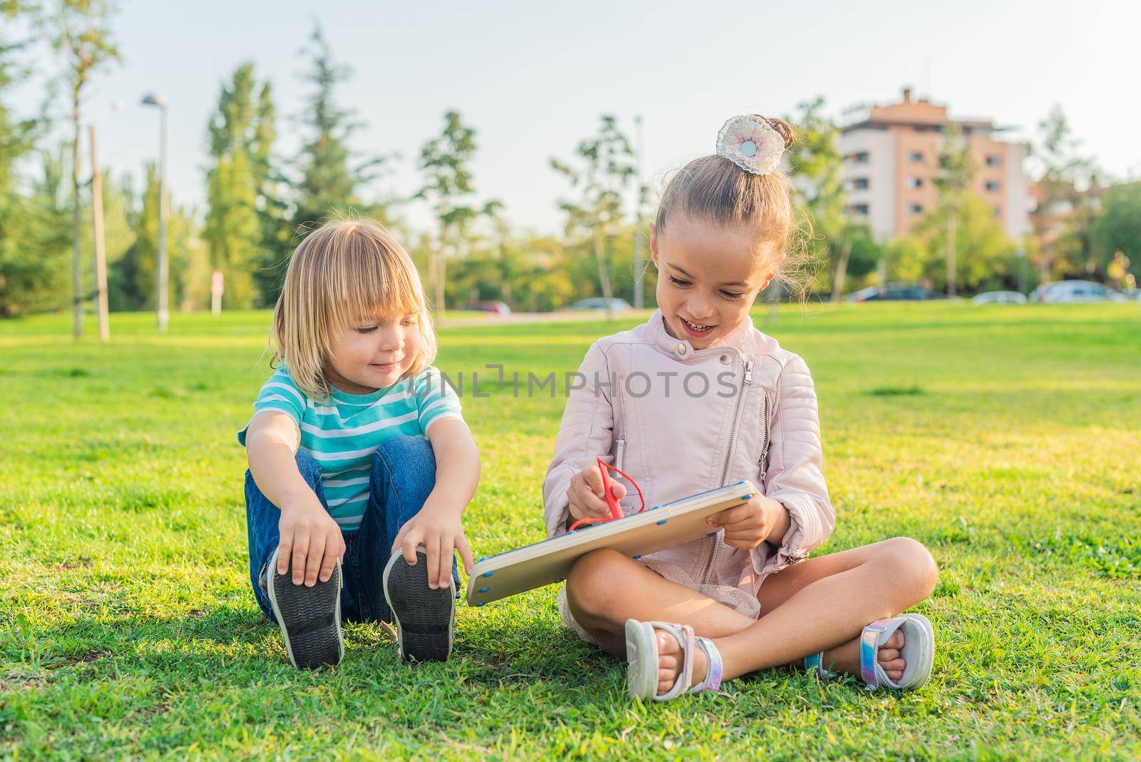 girl and brother sitting on the grass in a park by ivanmoreno