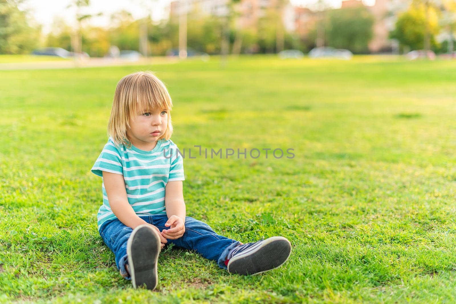 Full length view of a little boy sitting on grass of a park looking away with copy space