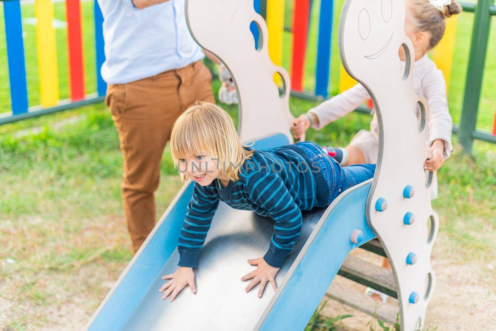 Portrait of a little boy playing slider at playground with his little sister.