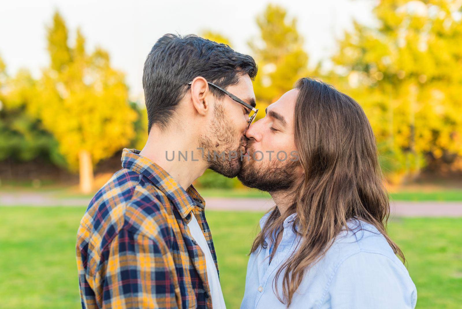 Side view of a young gay male couple kissing in the park.