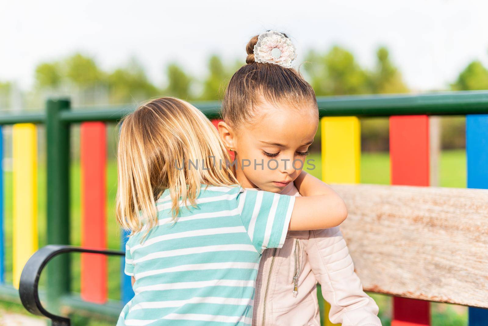 A little caucasian blond boy on his back cuddles and apologizes to his little sister for misbehaving with her outdoors.