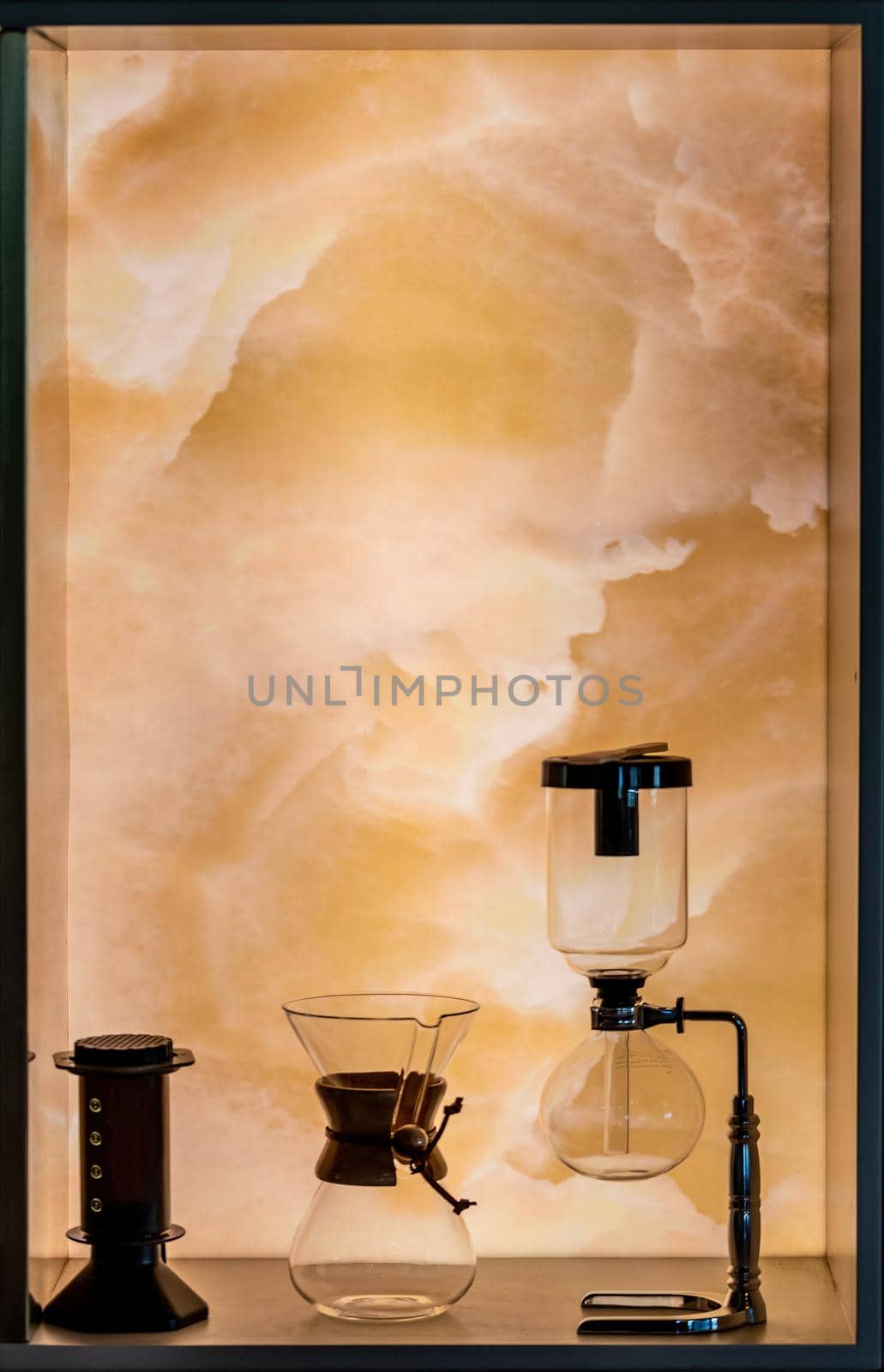 Alternative third generation coffee brewing equipments standing on the illuminated shelf. Selective focus by Sonat