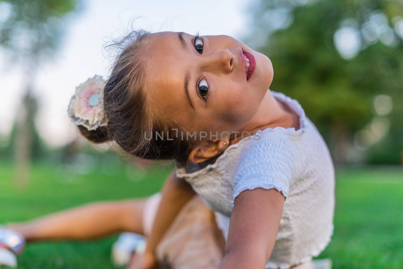 Portrait of a girl lying on her side on the grass with her back curled up and looking at the camera.