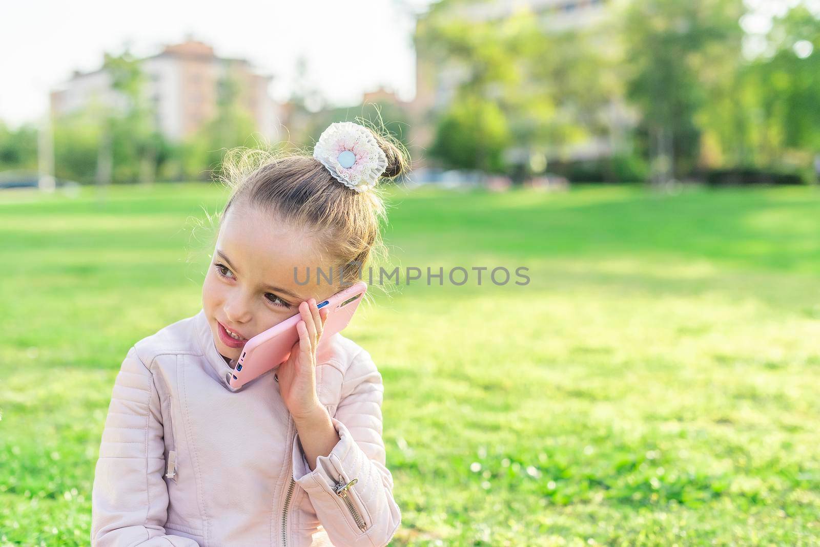 Front view of a little girl looking away talking on phone in the park with copy space.