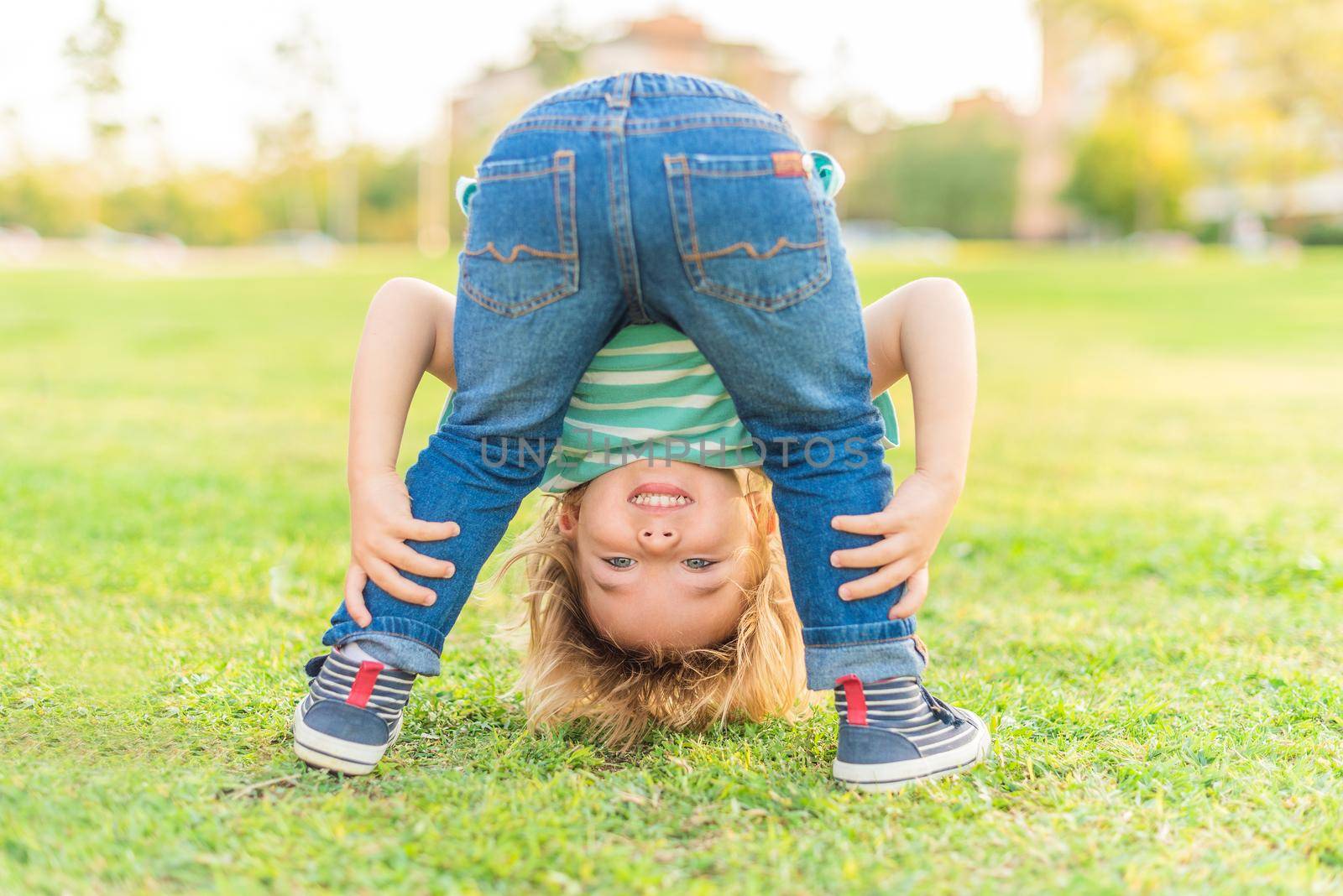 Front view of a playgul little boy standing looking through his own legs at the camera in the park.