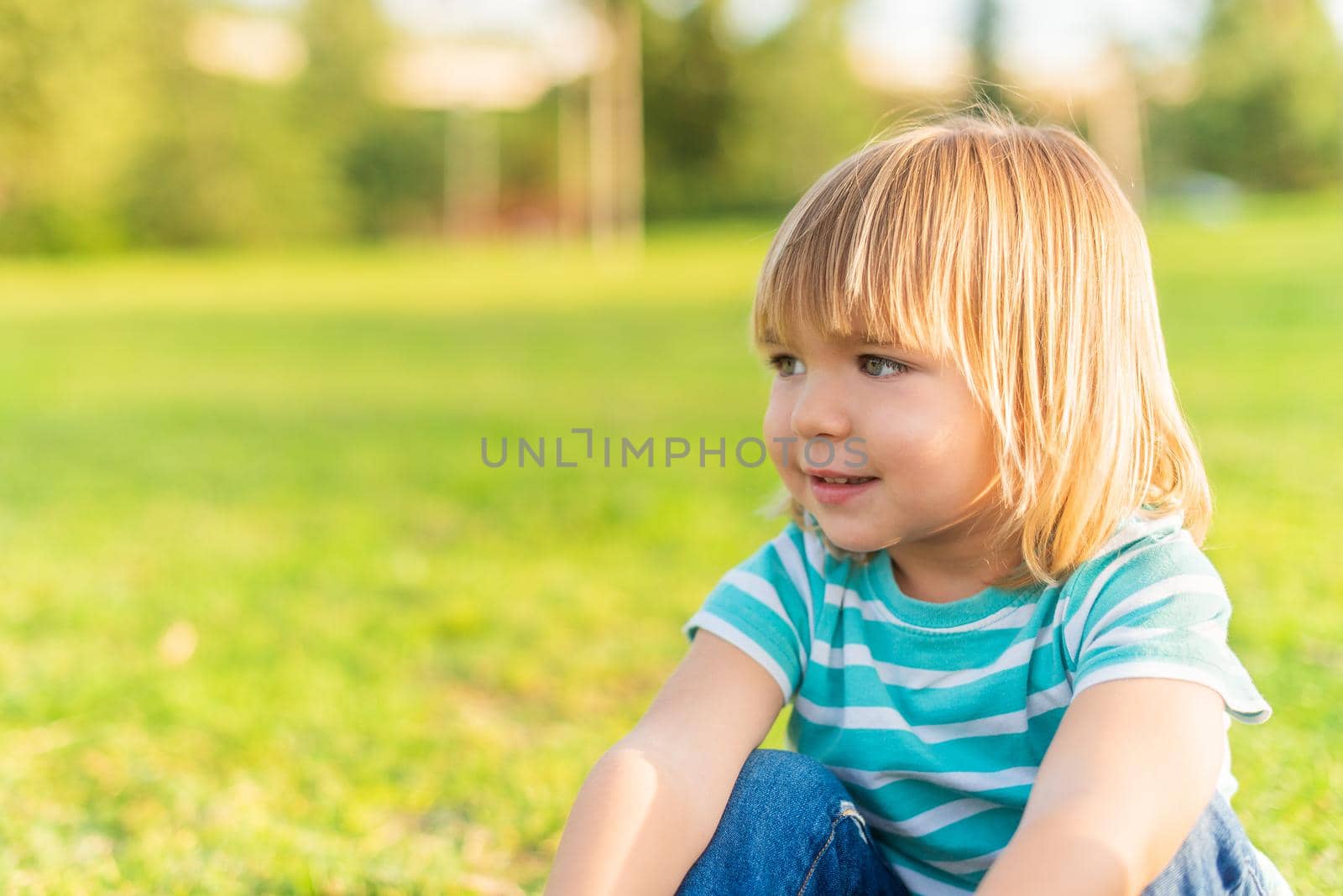 Portrait of a little boy sitting on grass in a park looking away with copy space