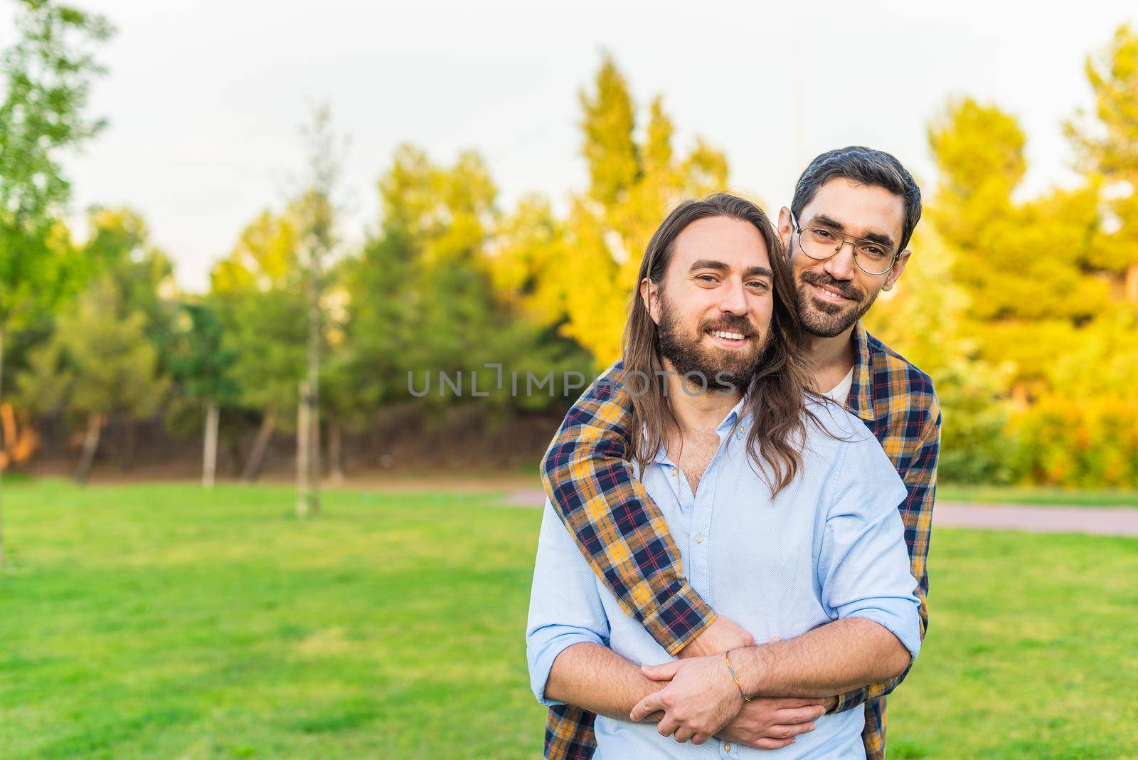 Front view of a gay couple looking at camera hugging in the park with copy space.