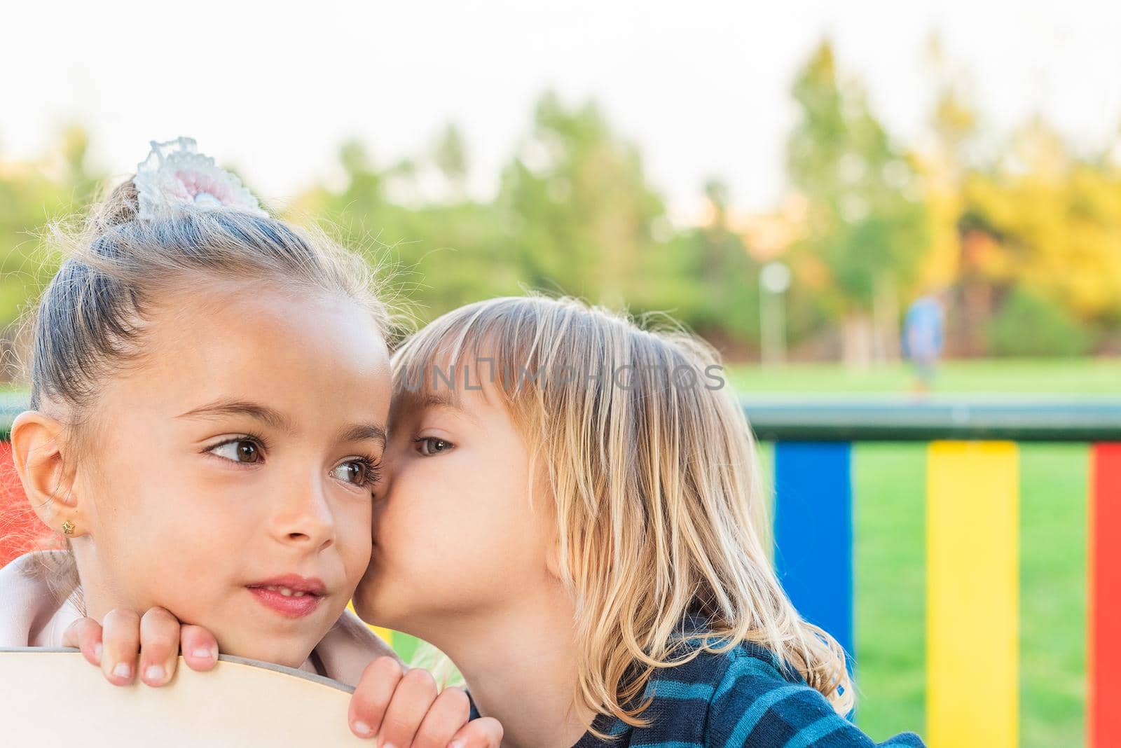 Front view of a little boy whispering something to his little sister in the playground