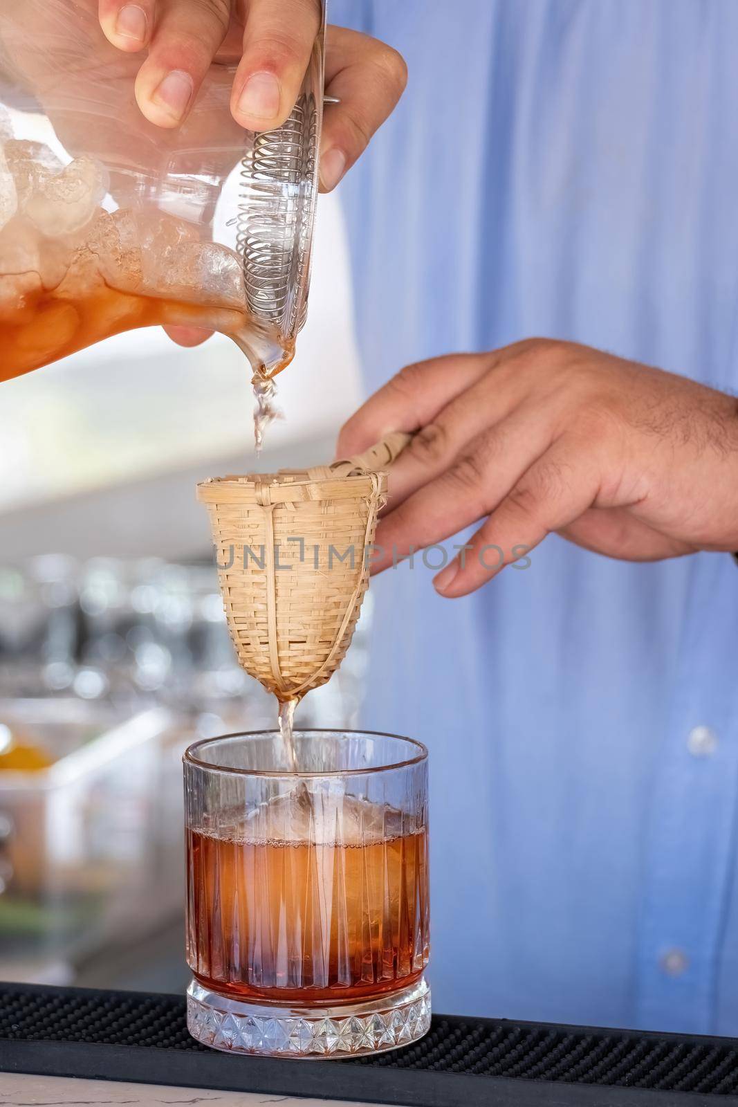 Professional bartender pouring cocktail into glass glass with shaker