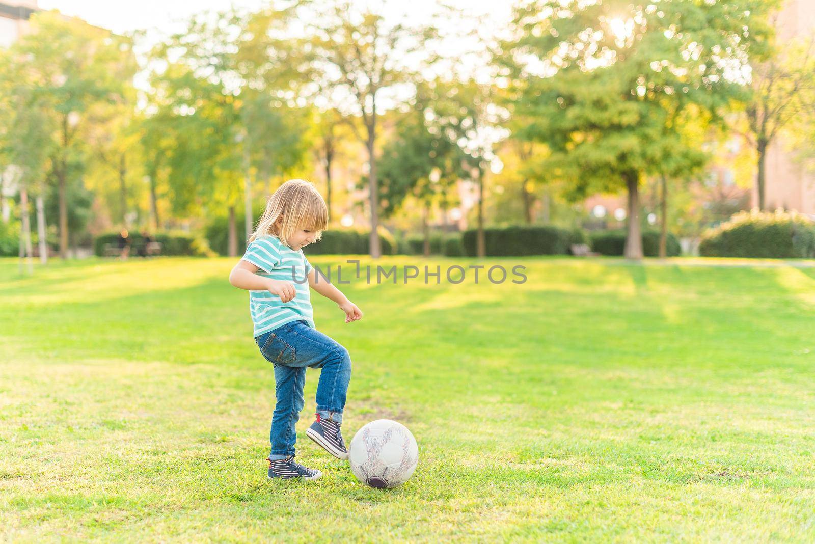 Full length view of a little boy playing with a ball on grass in park in a sunny day.