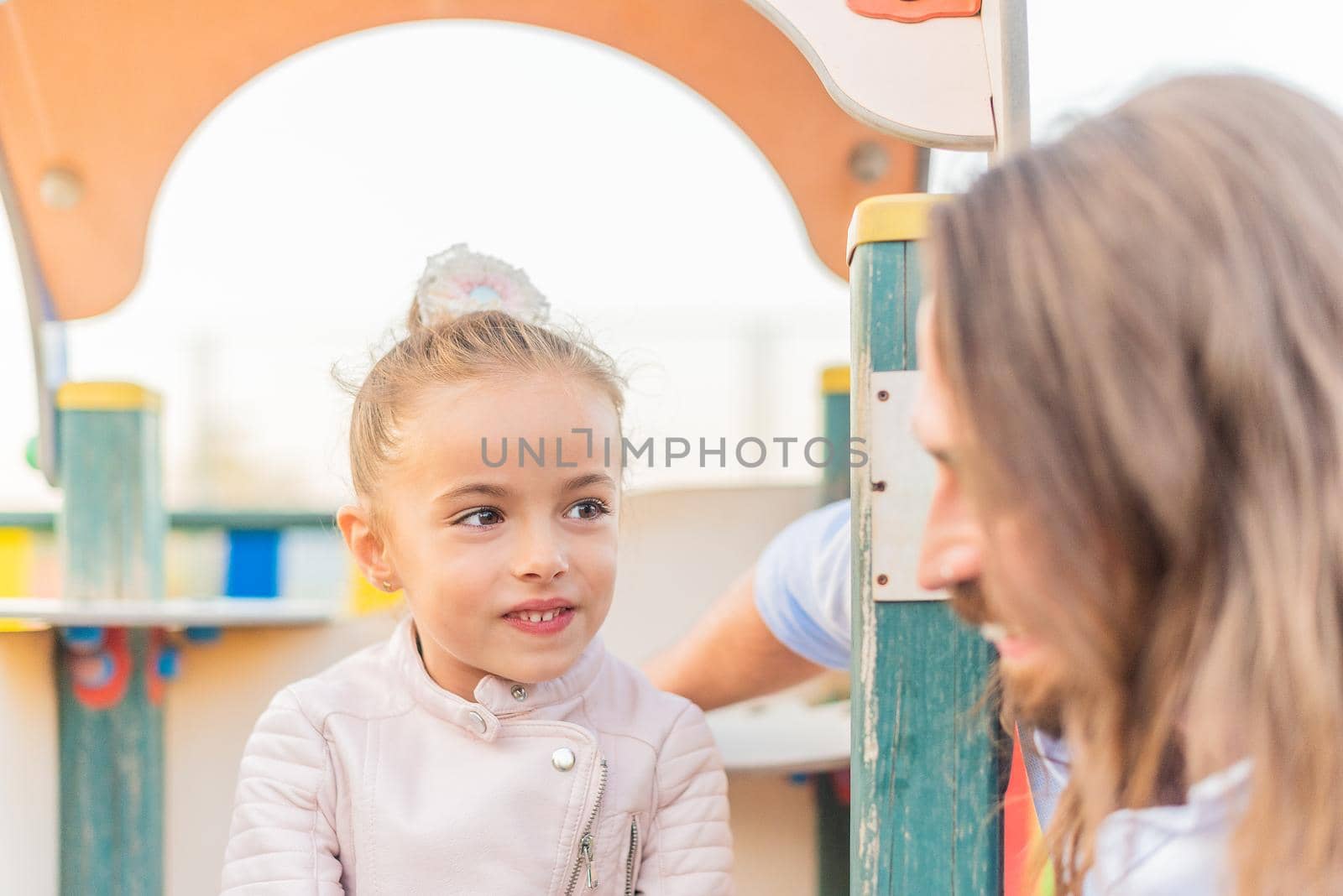 Front view of a little daughter smiling and looking to her young dad in the playground