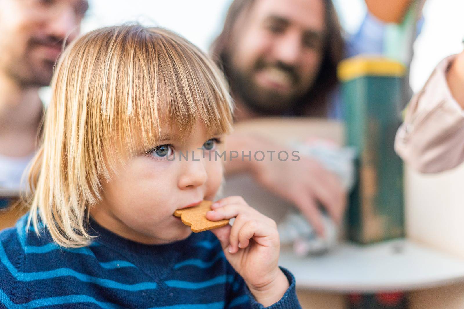 Close up view of a little boy eating a cookie with his family in blurry background