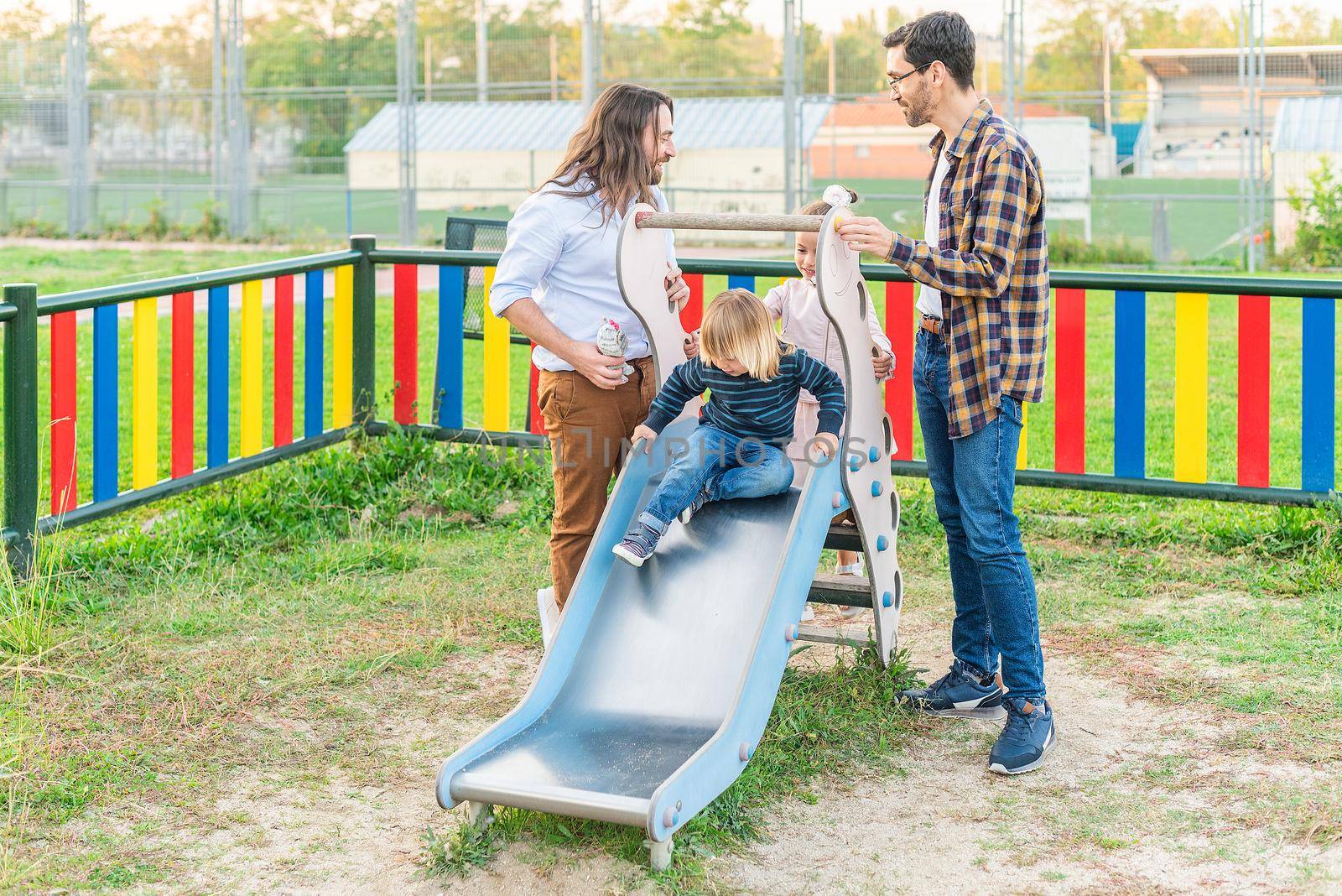 gay male couple playing with their children on the slider by ivanmoreno