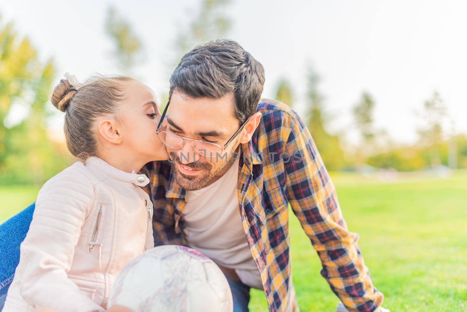 Front view of a cute little girl kissing her single father on cheek in a park in a sunny day.