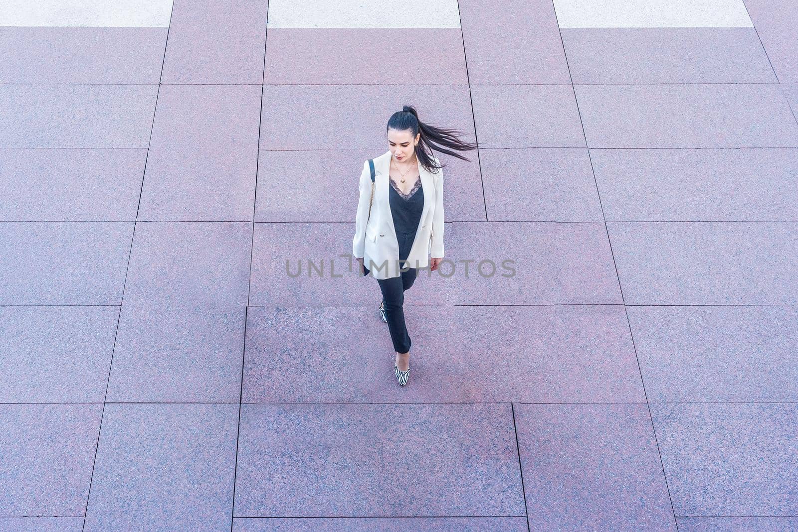 woman in white jacket walking with ponytail swinging, view from above