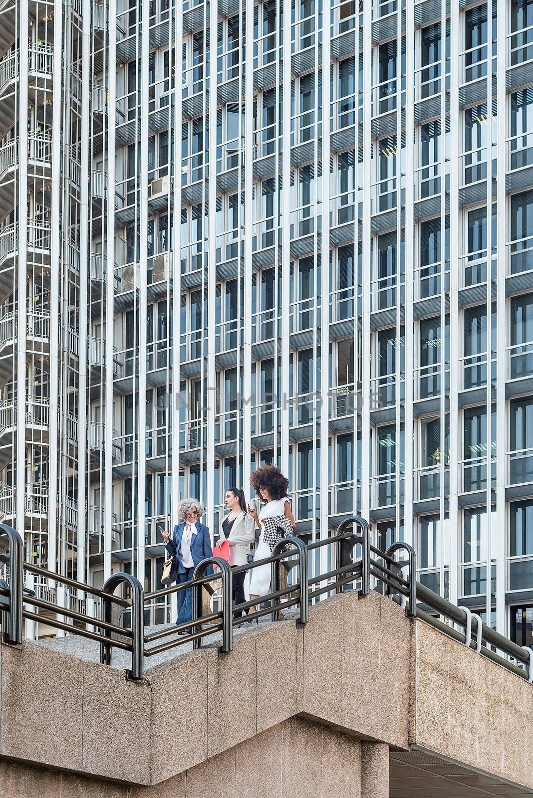 view from below of three female workers on a staircase, tall building in the background