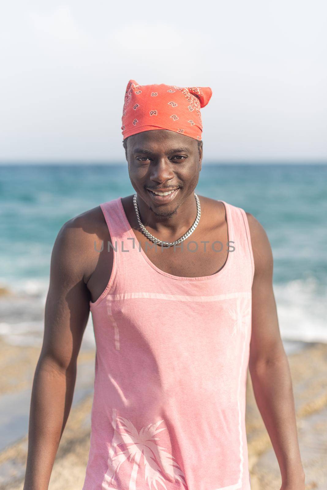 portrait of a black man in a pink t-shirt with the beach in the background, vertical picture