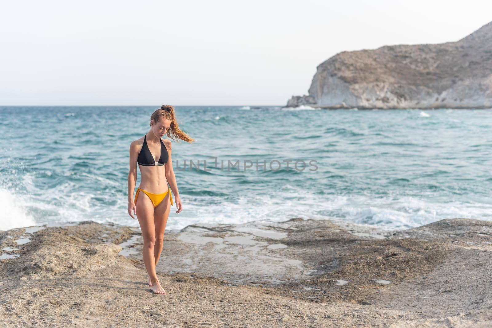 white woman in swimsuit thinking and moving along the beach shore, horizontal picture