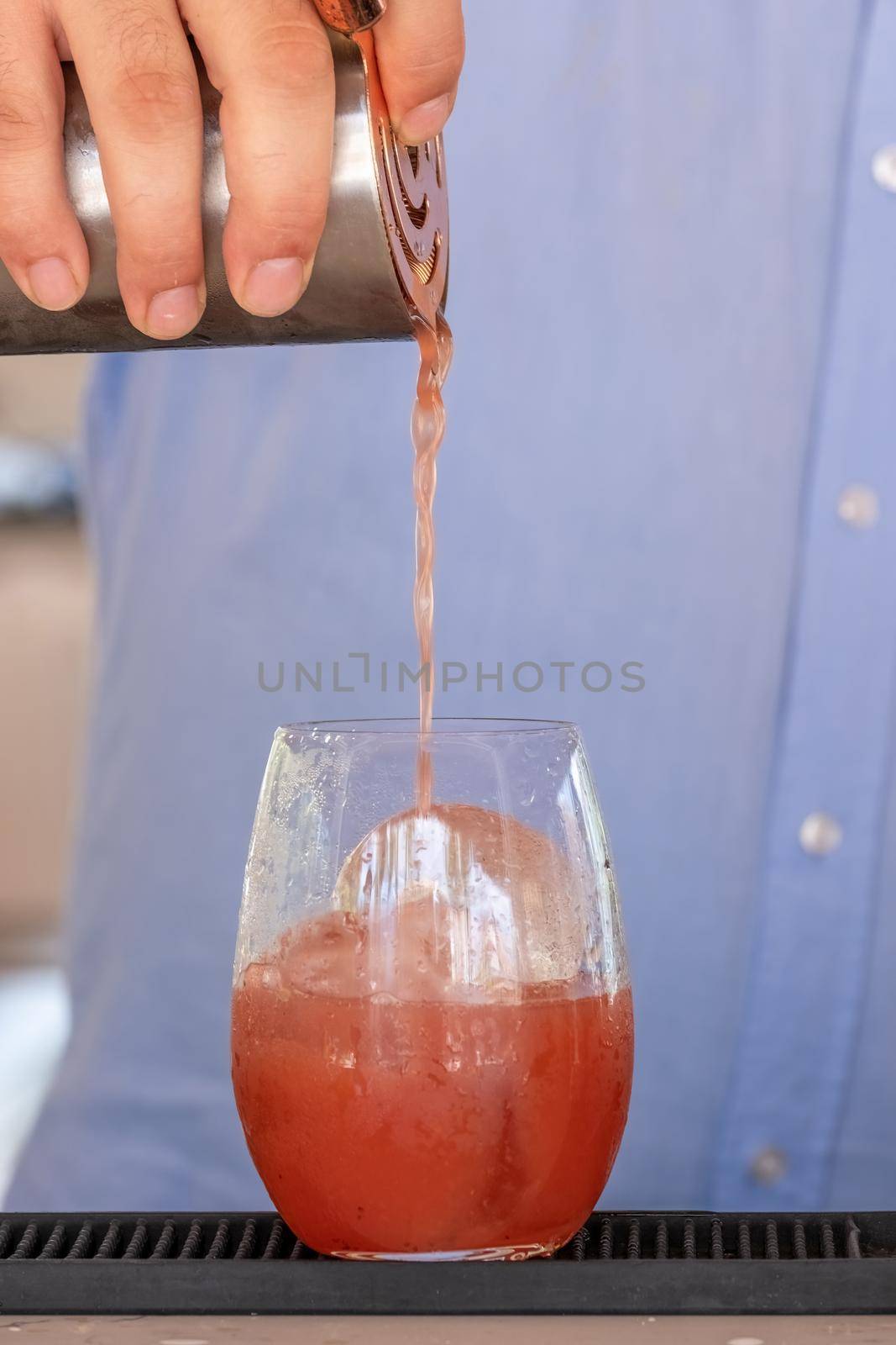 Professional bartender pouring cocktail into glass glass with shaker